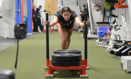 Girl student pushing weights on sled in weight room