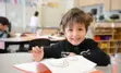 A young smiling student writing at their desk.